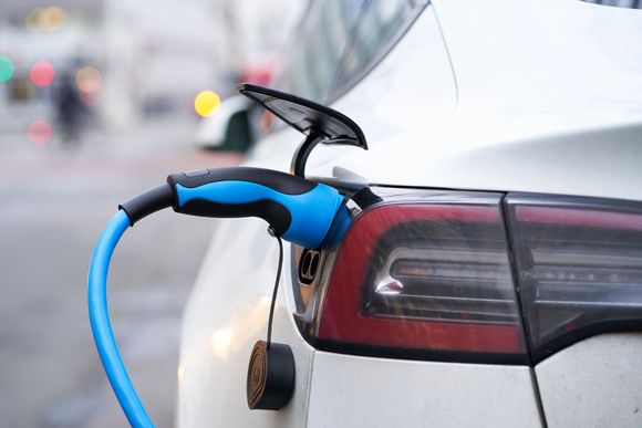 Cavo di ricarica blu per veicoli elettrici collegato a un'auto bianca presso una stazione di ricarica.