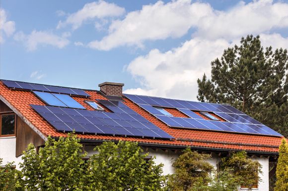 Il tetto della casa è ricoperto di pannelli solari blu sotto un cielo parzialmente nuvoloso.