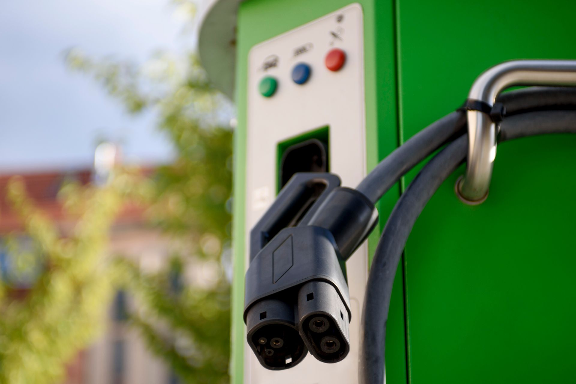 Spina di ricarica per veicoli elettrici collegata a una stazione di ricarica verde all'aperto.