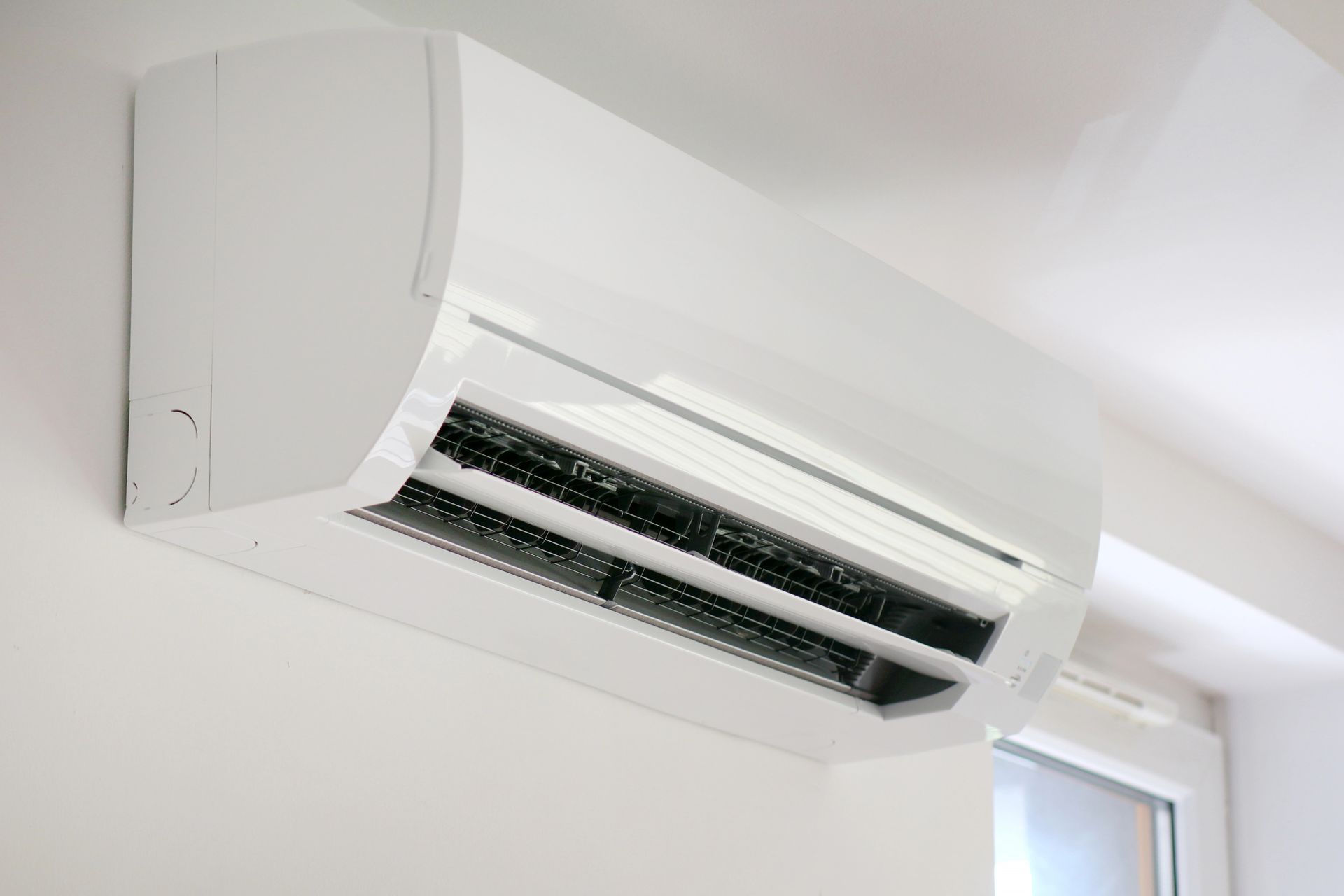 Condizionatore d'aria bianco a parete, posizionato vicino a una finestra luminosa all'interno.