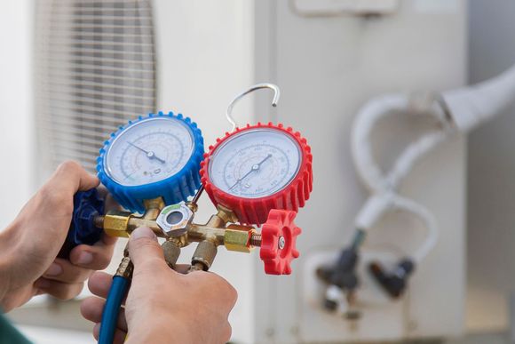 Mani che reggono manometri blu e rossi per impianti di climatizzazione durante la manutenzione.