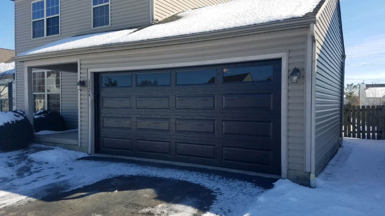 Snowy suburban driveway with a dark two-car garage door attached to a house
