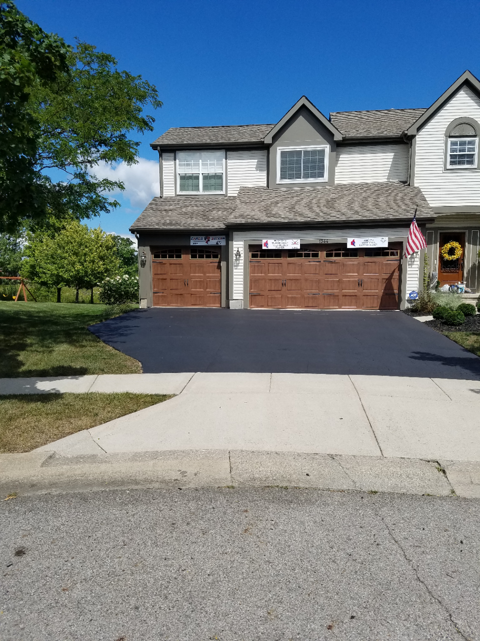 Suburban two-story townhouse with two wooden garage doors, driveway, and a small front lawn under a clear sky