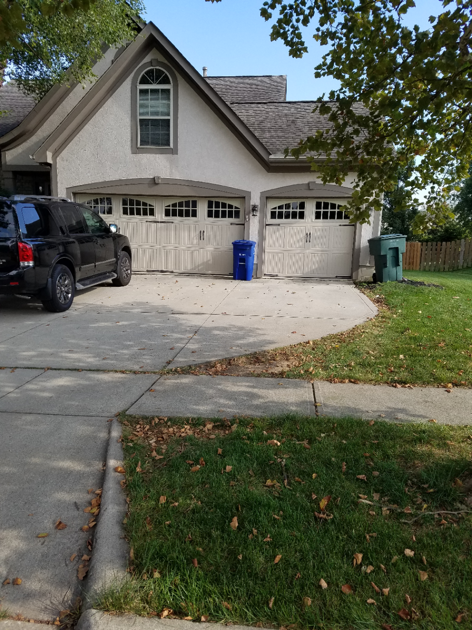 Suburban house with two garages, a black SUV in the driveway, and a blue recycling bin by the door