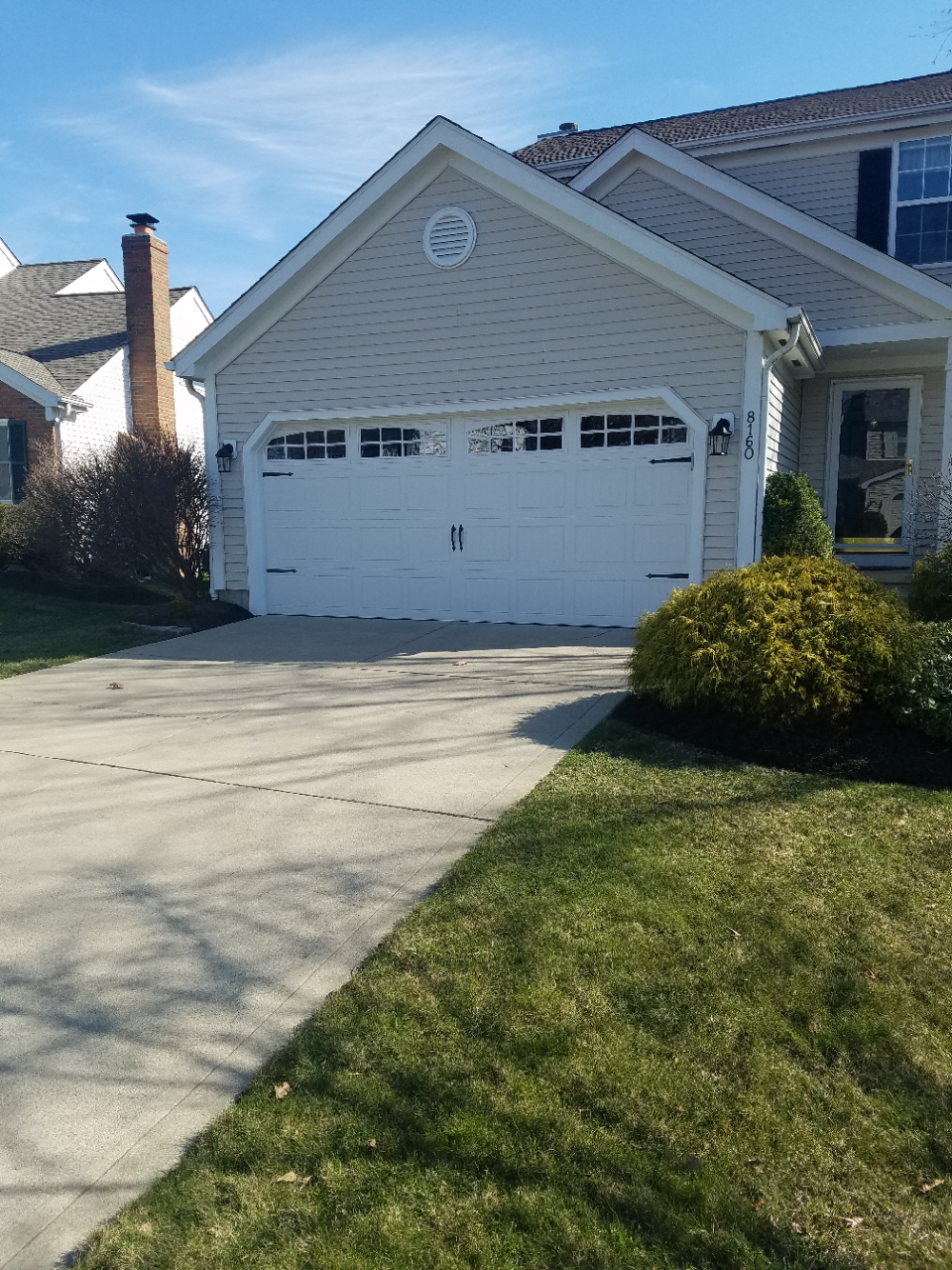Suburban house with white garage, driveway, and front lawn on a sunny day