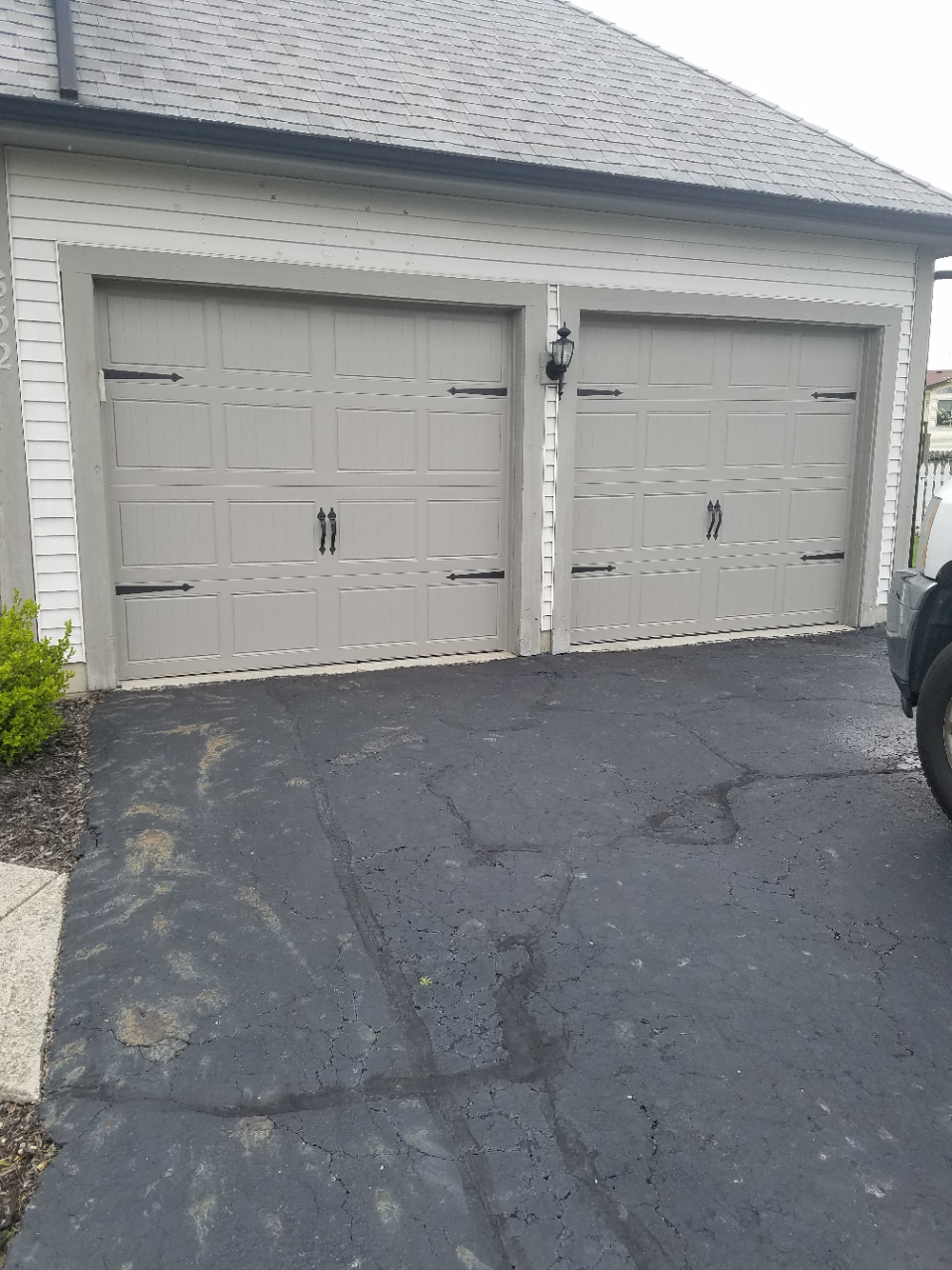 Two-car garage with white doors and a cracked asphalt driveway in front of a house