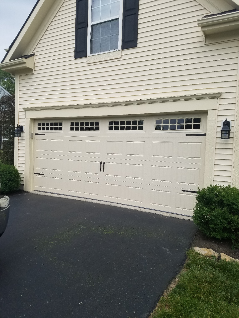 White double garage door on a beige house with black shutters and a dark driveway