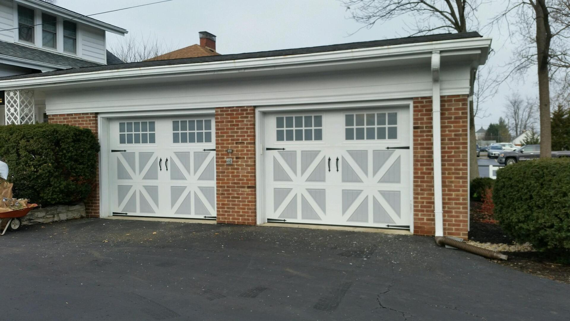 Two white garage doors on a brick house with white trim and a black driveway