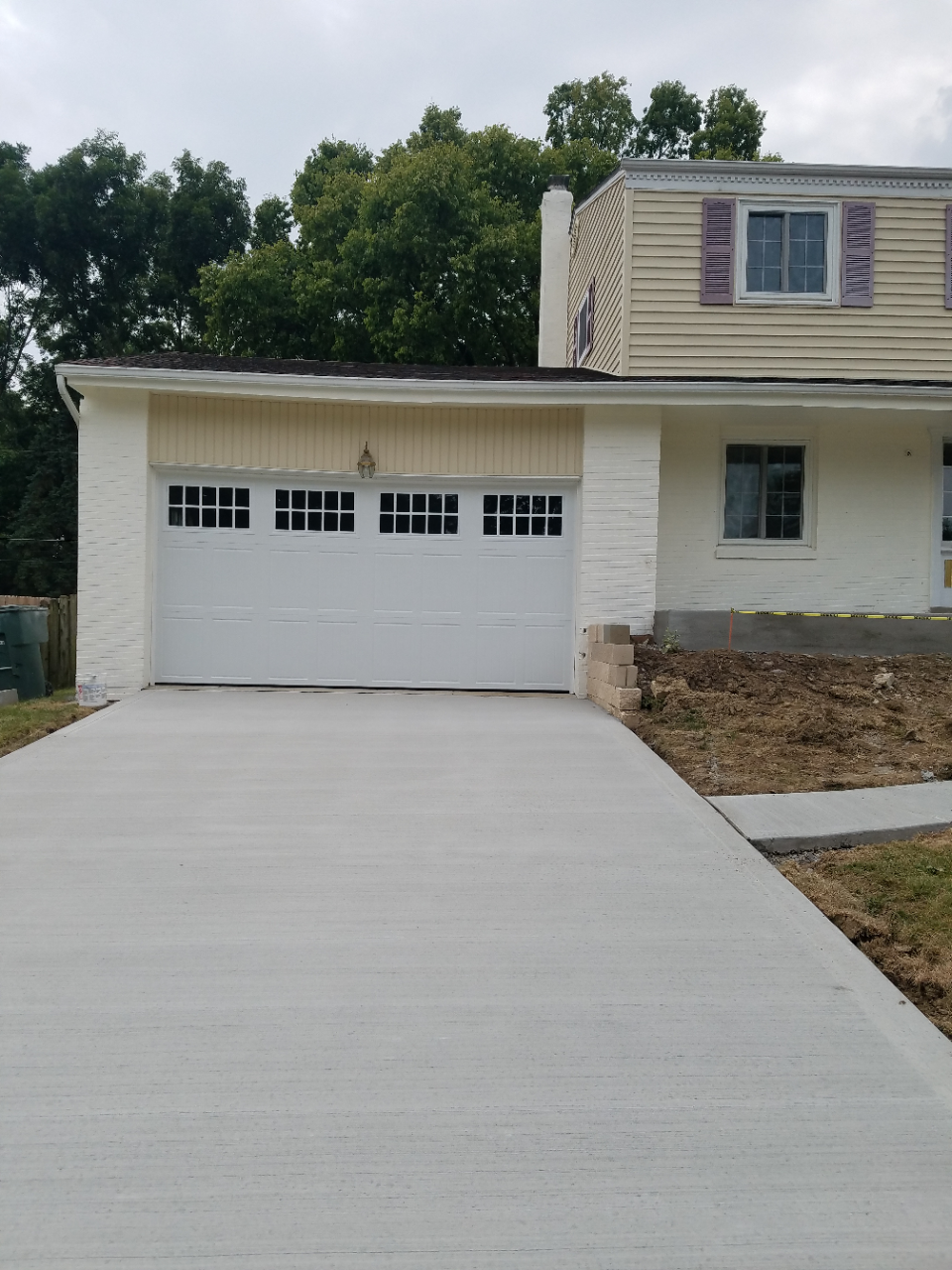 White garage with concrete driveway beside a beige house and stone retaining wall