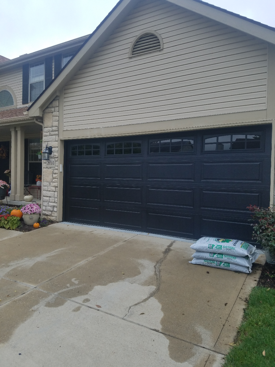 House exterior with a dark double garage door, wet driveway, and bags of mulch by the garage.
