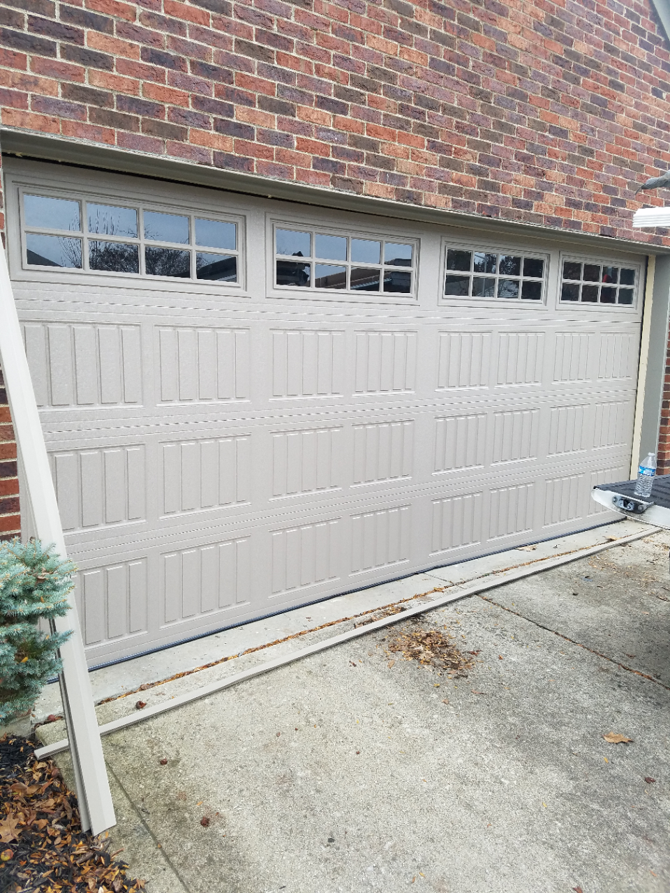Gray garage door with small windows set in a brick exterior wall, viewed from a driveway.