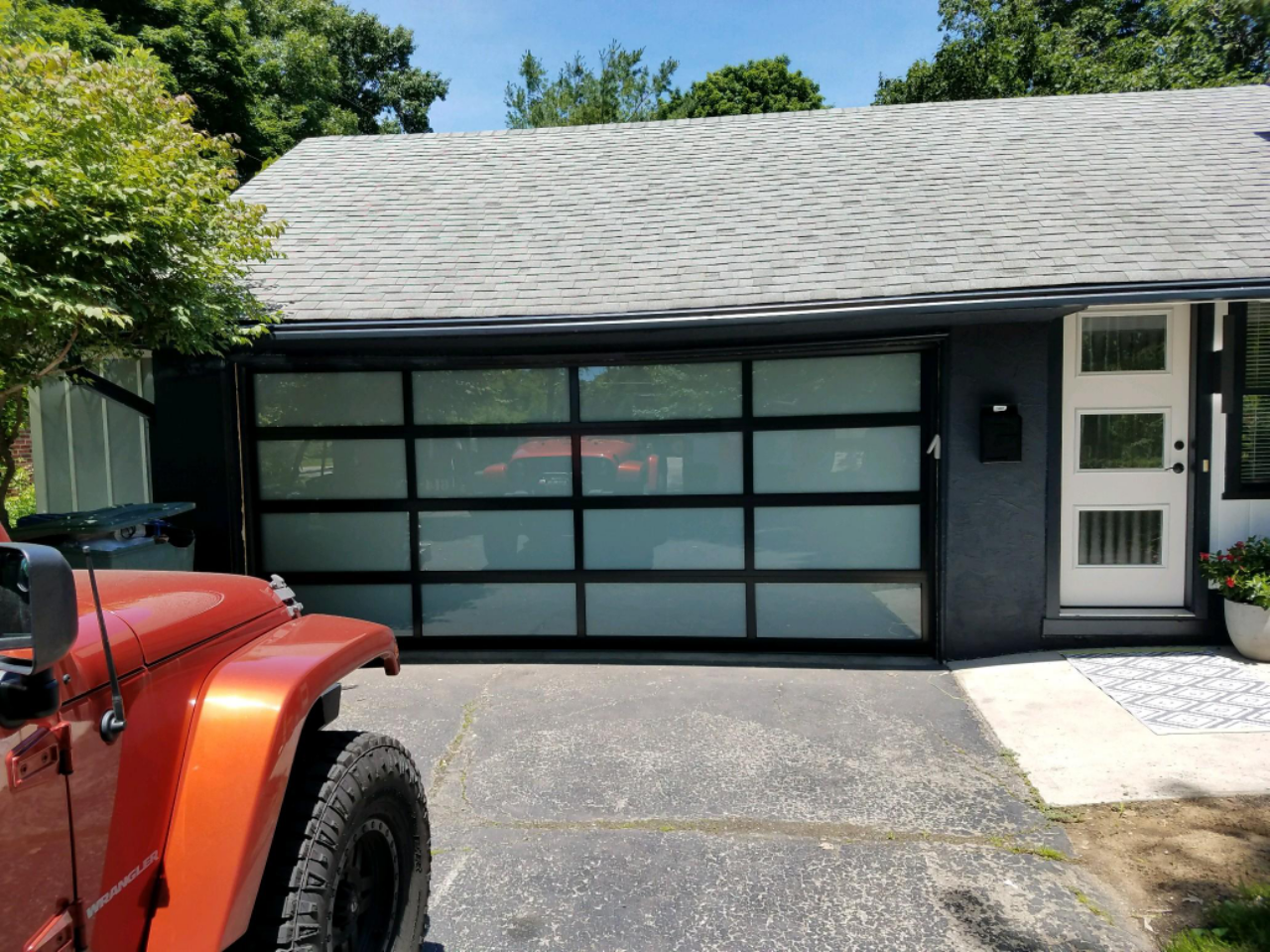 Modern black garage with frosted glass door, white side entrance, and red vehicle at left.