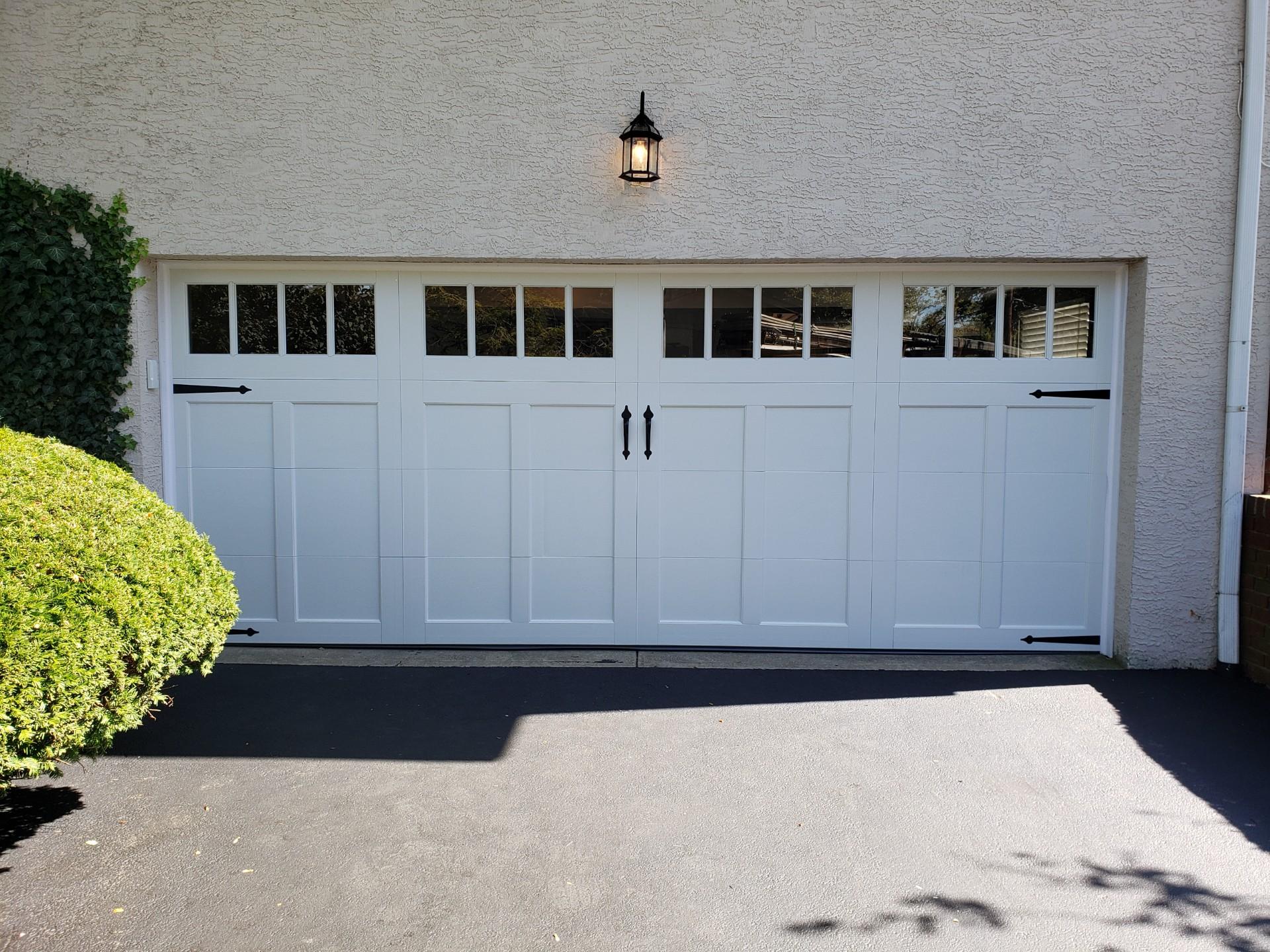 White garage door with small windows on a stucco house, lit by a wall lantern.