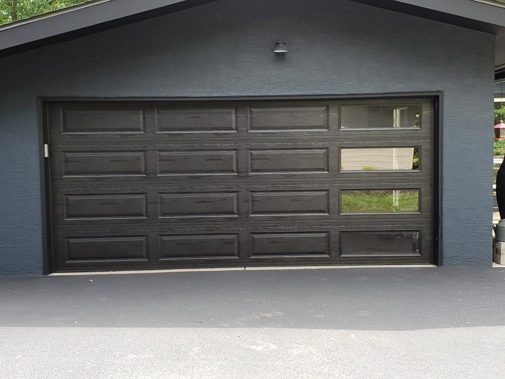 Black garage door on a dark gray house with a small window panel on the right.