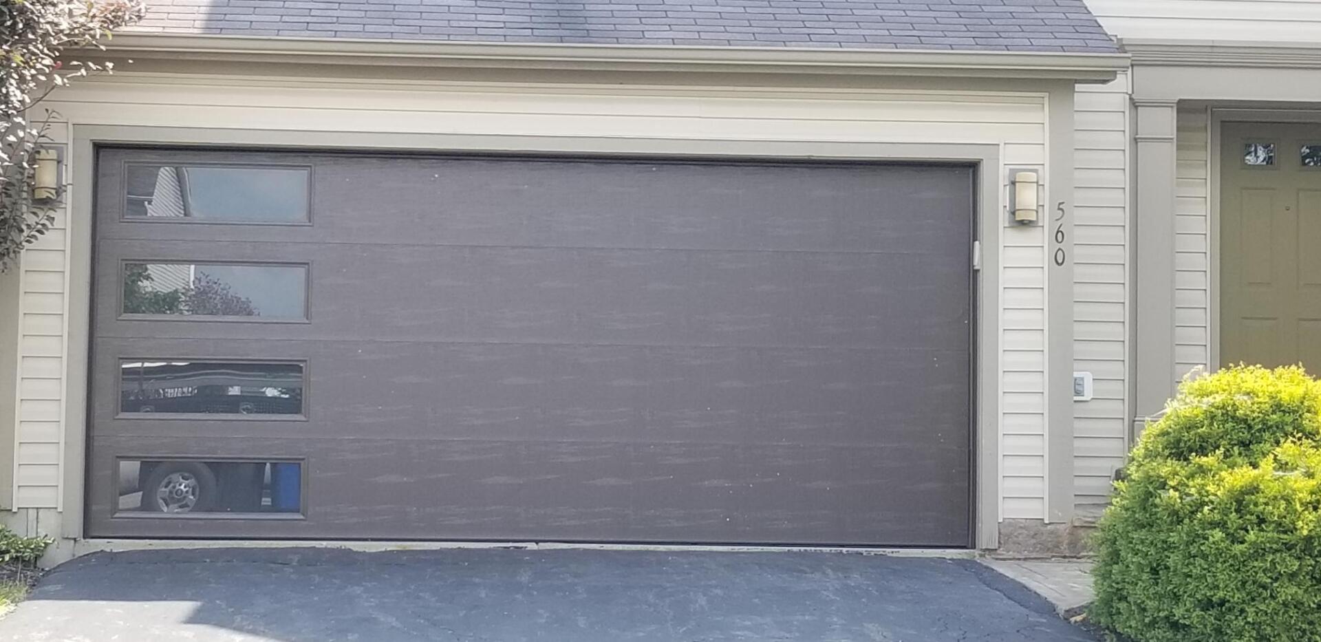 Gray garage door on a suburban house with three narrow windows and trimmed bushes nearby
