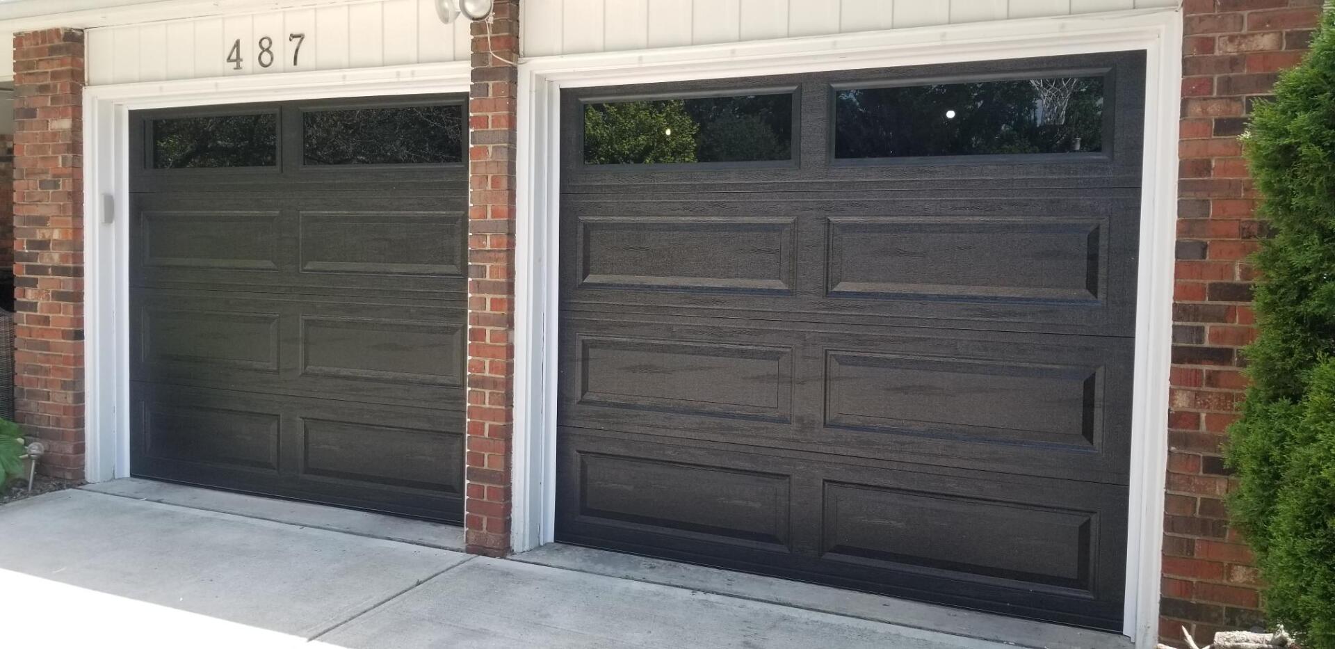 Two dark garage doors on a brick house with the number 487 above them