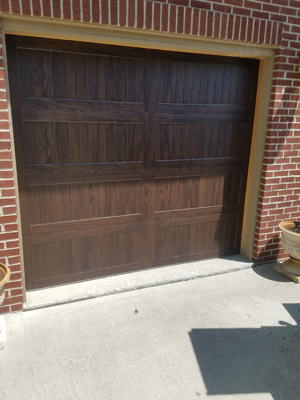 Wooden garage door set in a red brick exterior with a concrete driveway in front.