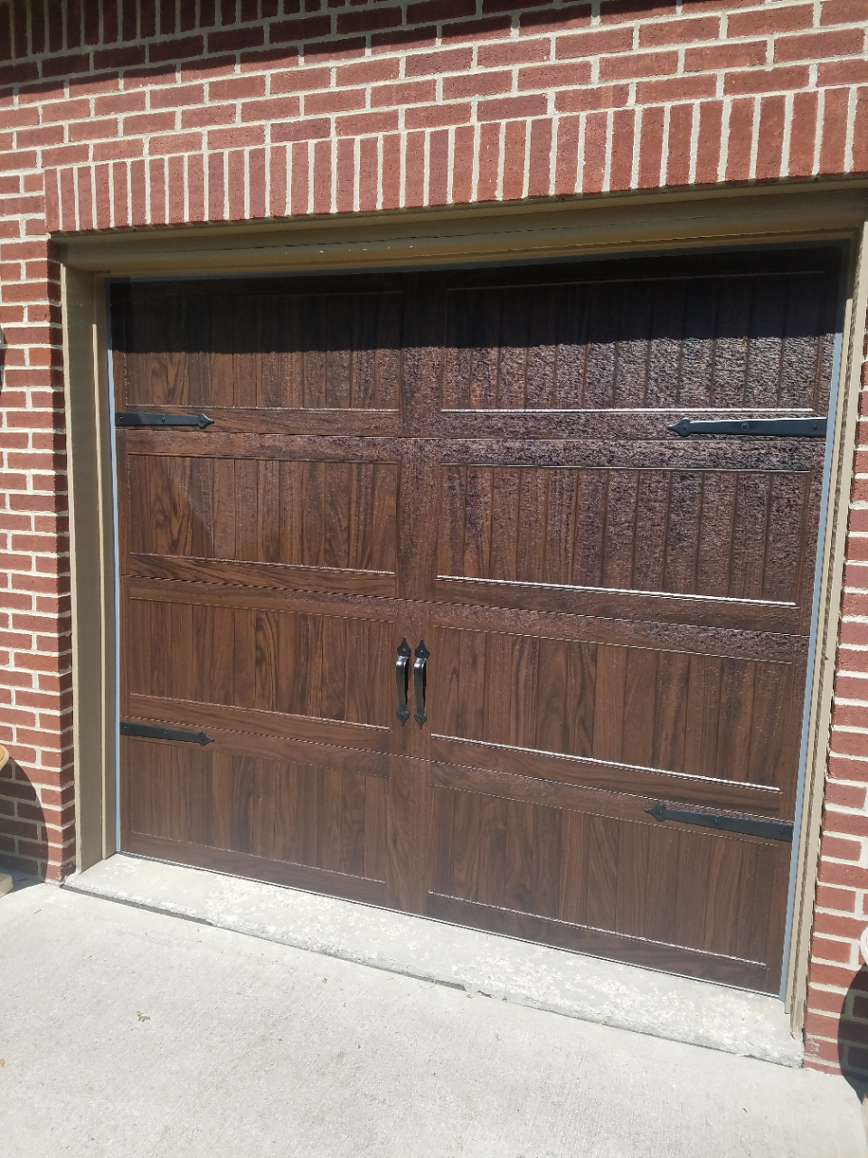 Dark brown wooden garage door set in a red brick wall, viewed from outside.