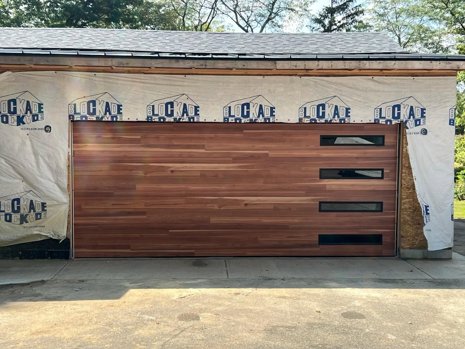 Modern wooden garage door installed in a cinder block wall, with exposed construction wrap above it.