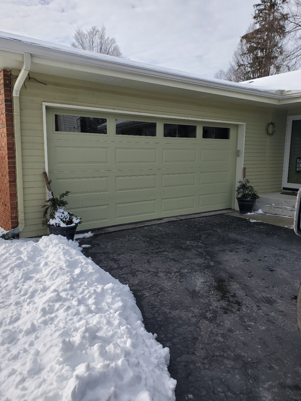 Snow-covered driveway in front of a green garage door on a house.