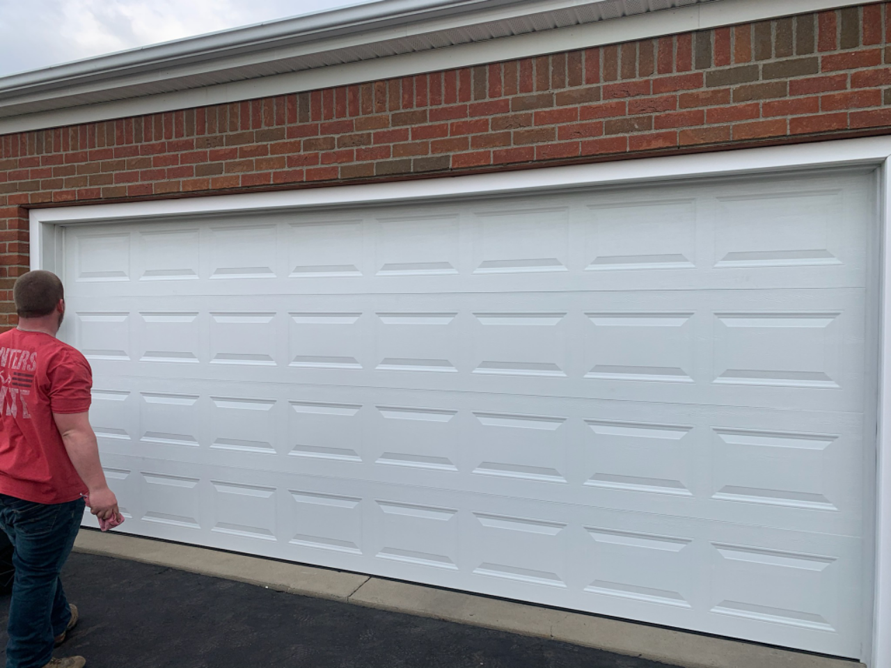 Man standing beside a white garage door on a brick building