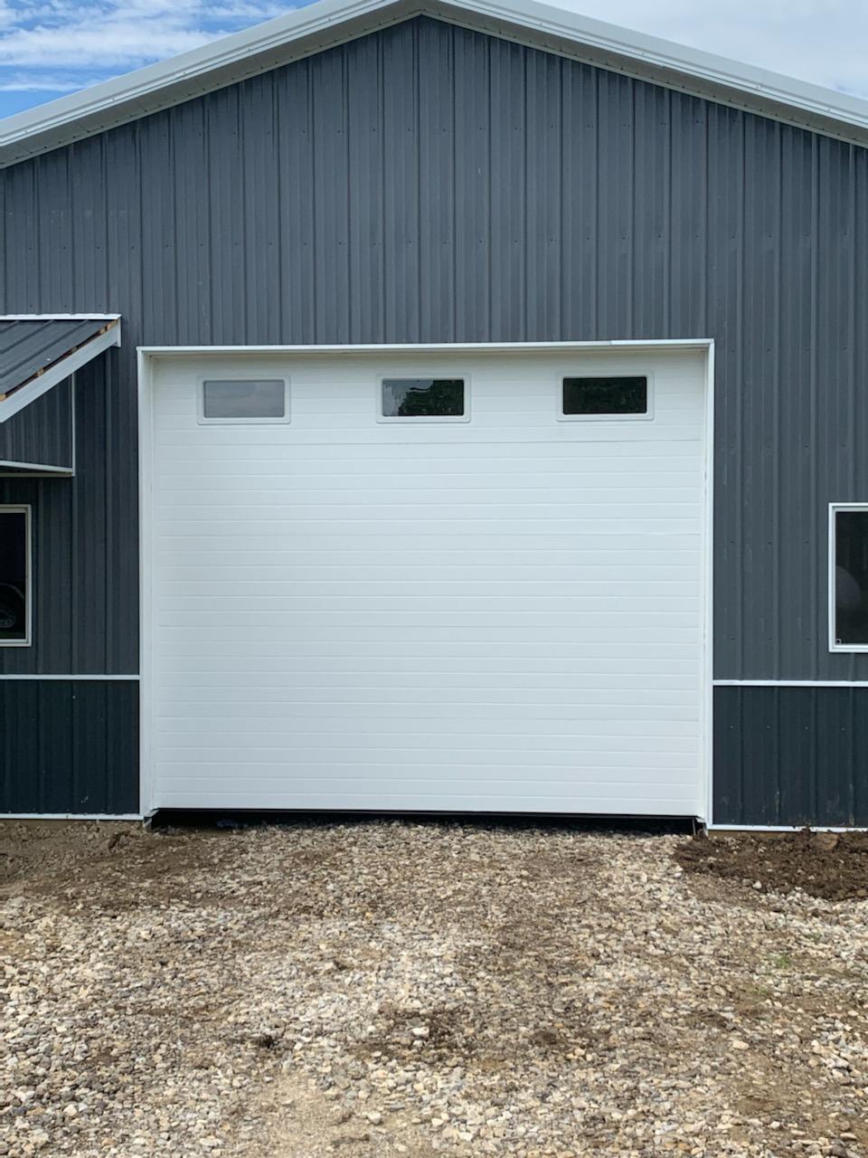 Gray metal building with a large white garage door and gravel driveway