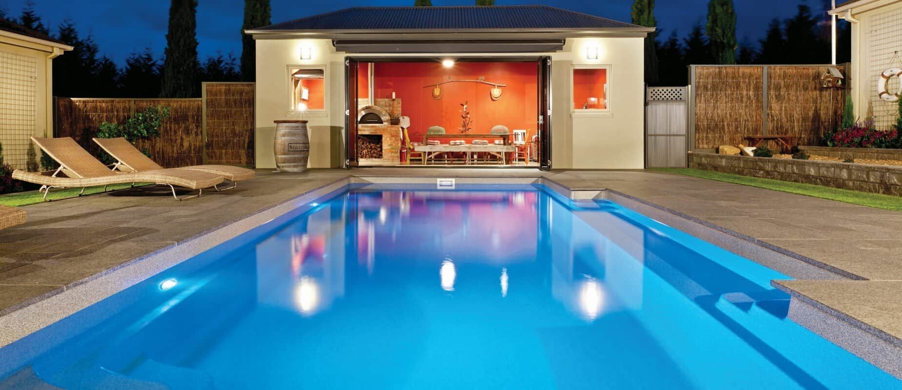 A Large Swimming Pool is Lit Up at Night in Front of a House — Azure Pools Mid North Coast In Old Bar, NSW