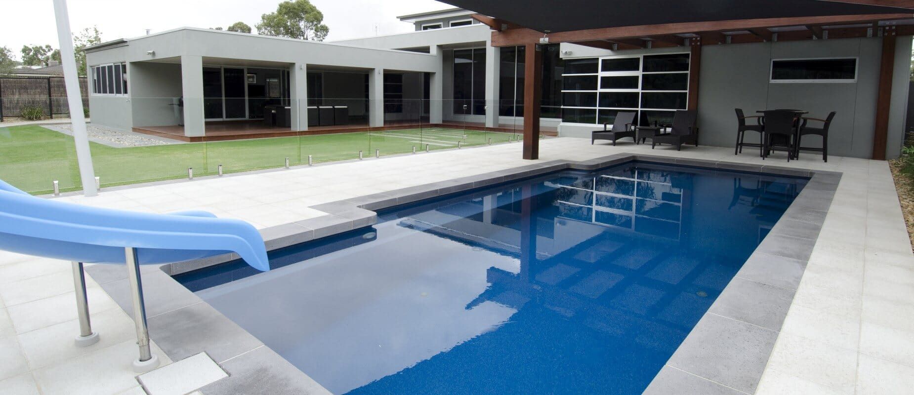 A Large Swimming Pool With a Slide and a House in the Background — Azure Pools Mid North Coast In Old Bar, NSW