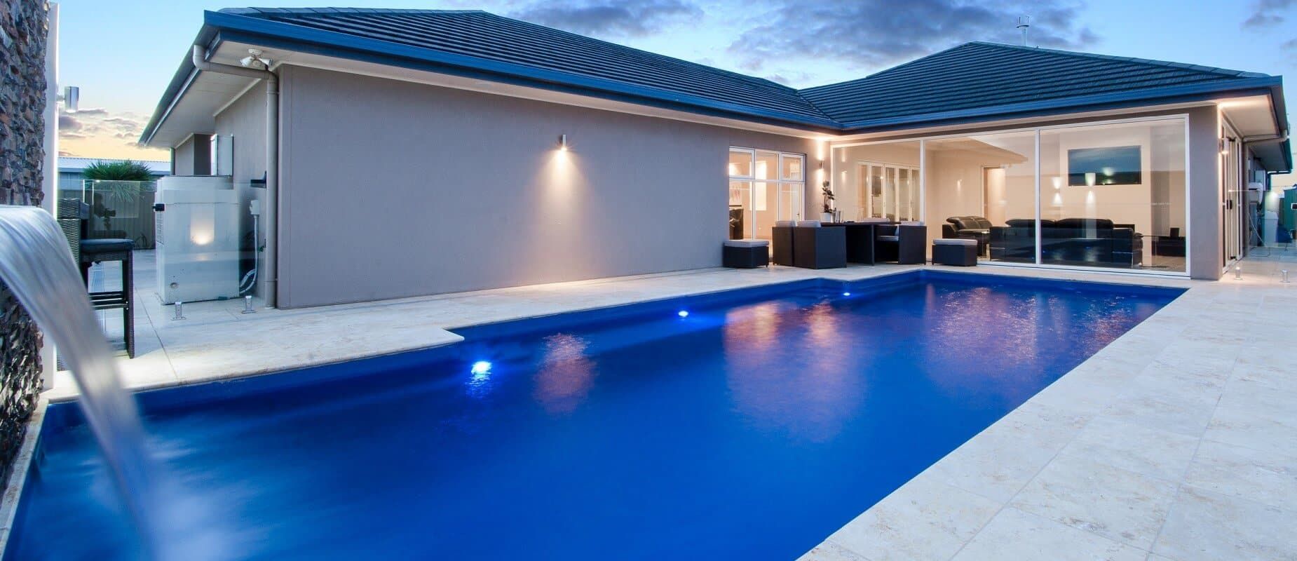 A swimming pool lit up at night with the house lights on behind it — Azure Pools Mid North Coast In Taree, NSW