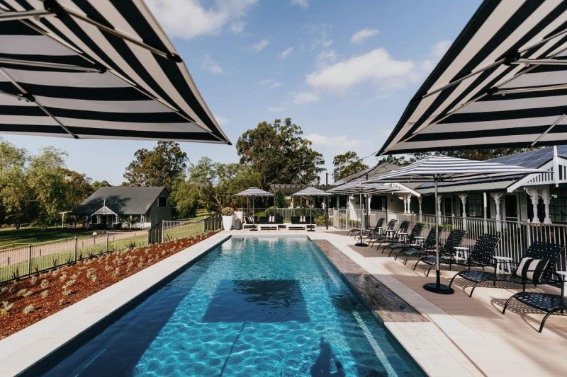 A Large Swimming Pool Surrounded by Chairs and Umbrellas — Azure Pools Mid North Coast In Taree, NSW