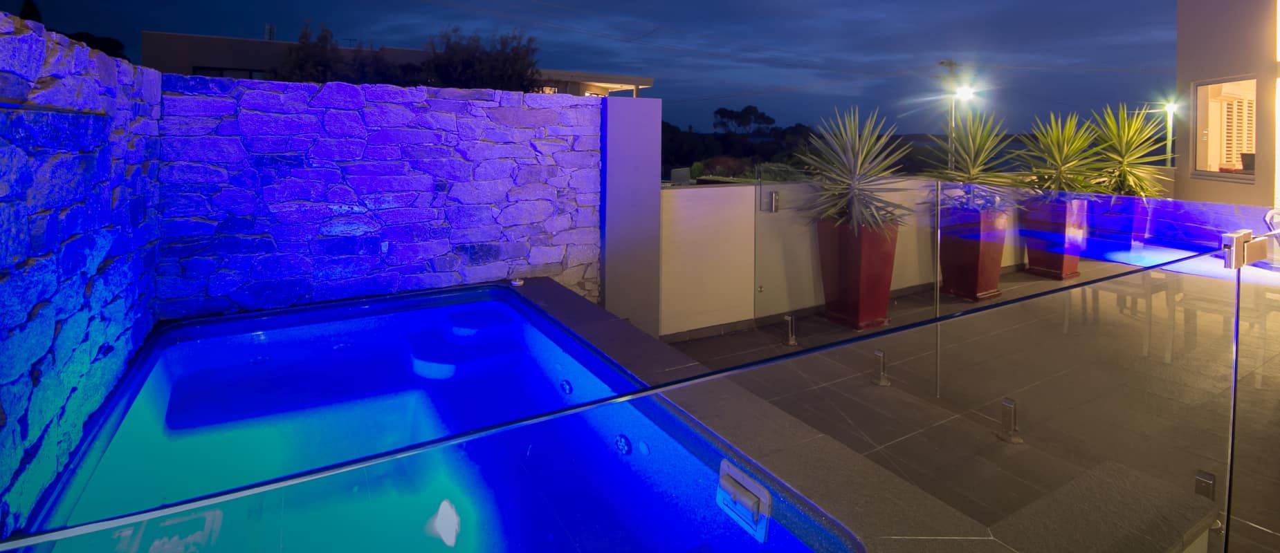 A Large Swimming Pool is Lit Up With Blue Lights at Night — Azure Pools Mid North Coast In Taree, NSW