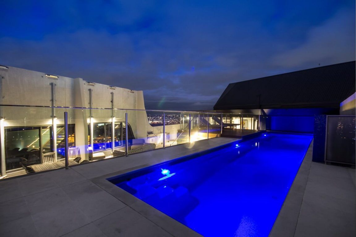 A Large Swimming Pool is Lit Up With Blue Lights at Night — Azure Pools Mid North Coast In Nabiac, NSW
