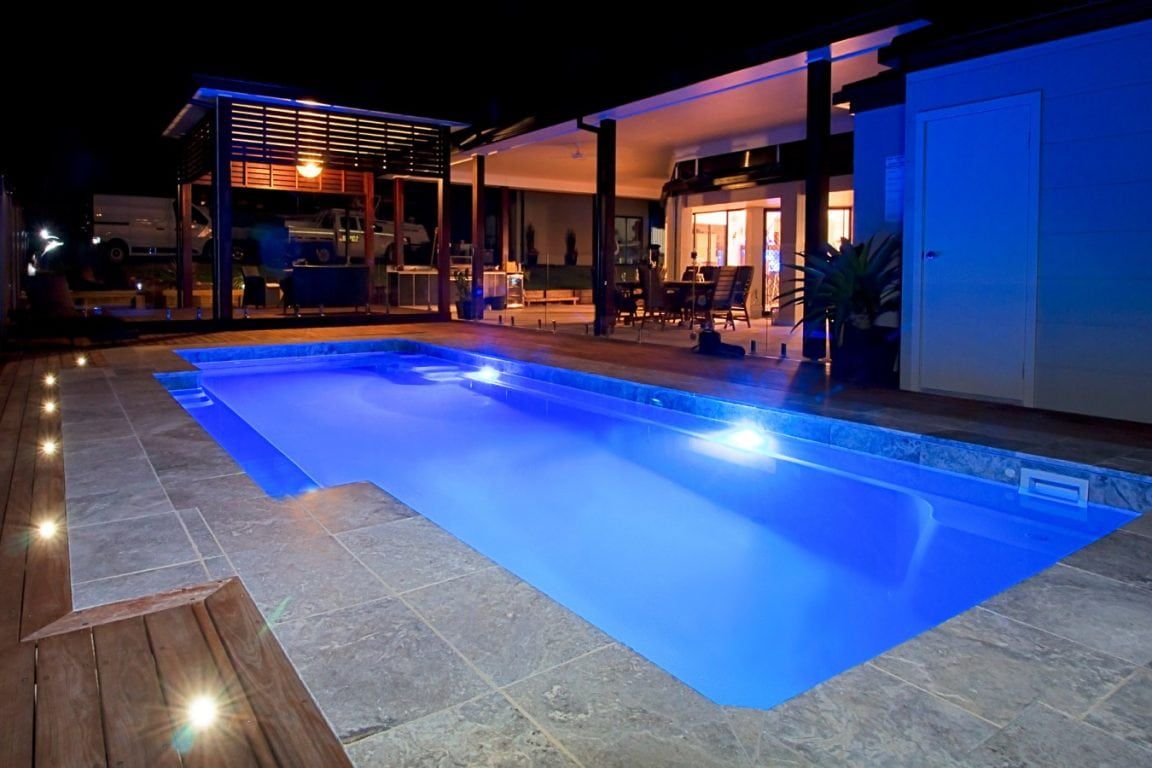 A Large Swimming Pool is Lit Up at Night in Front of a House That Has Lights On — Azure Pools Mid North Coast In Old Bar, NSW
