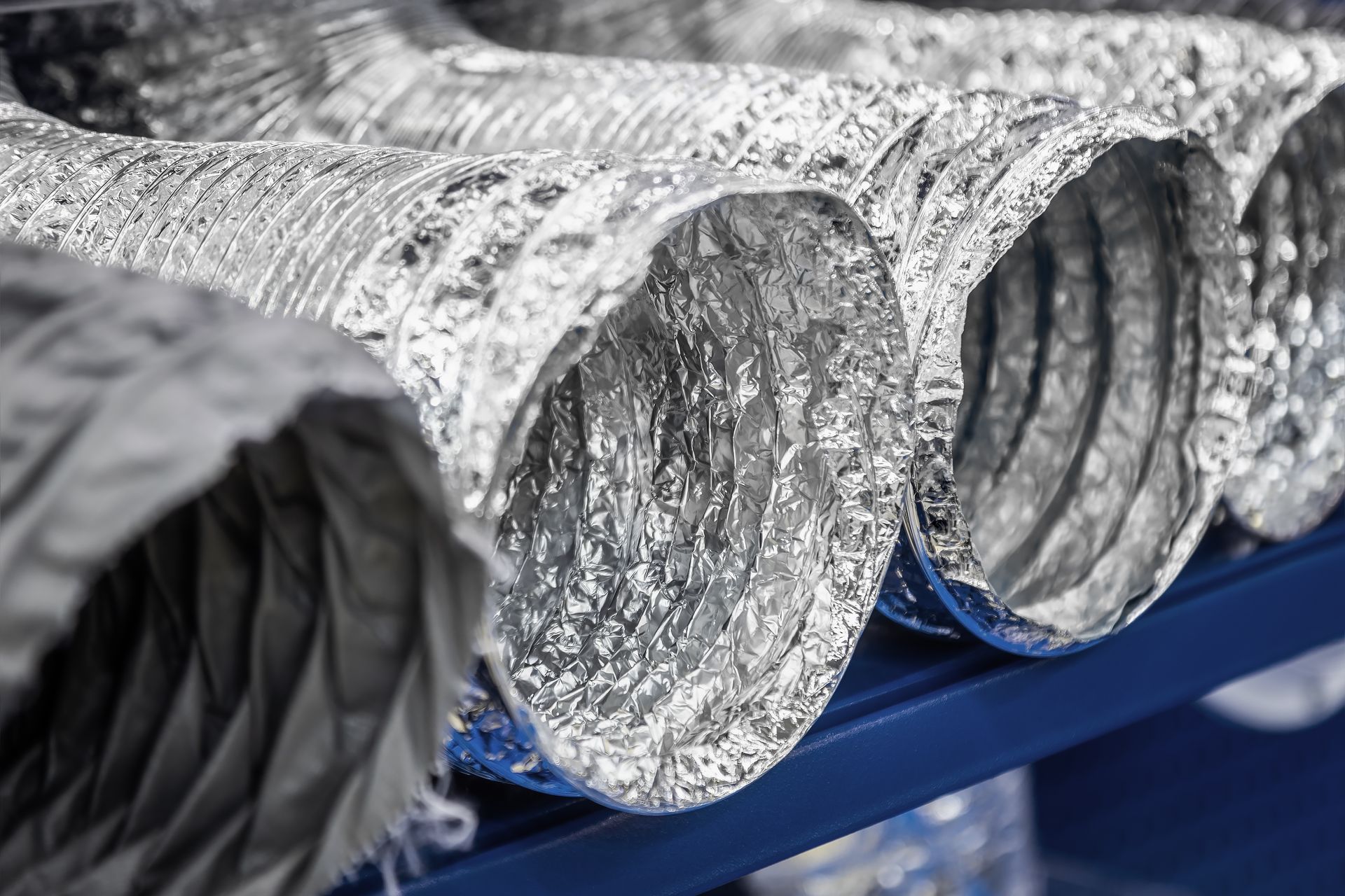 Silver, flexible metallic ventilation ducts resting on a blue shelving unit.