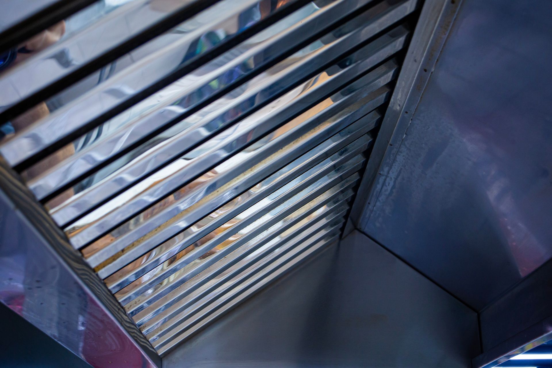 A close-up, angled view looking up into a clean, stainless steel kitchen range hood with its metal grease filters visible.