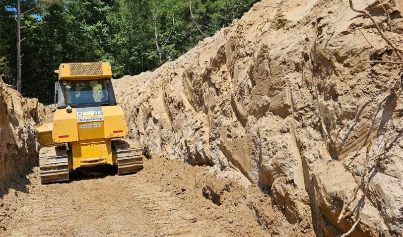 Yellow bulldozer on a dirt road beside a steep rocky excavation wall in a construction site