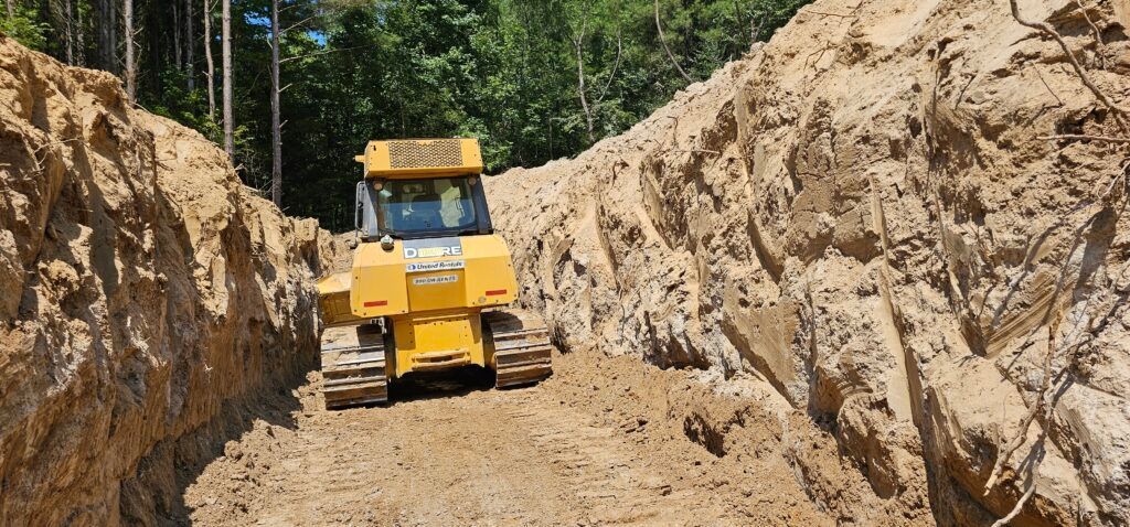 Yellow bulldozer grading dirt in a narrow trench between steep earth walls