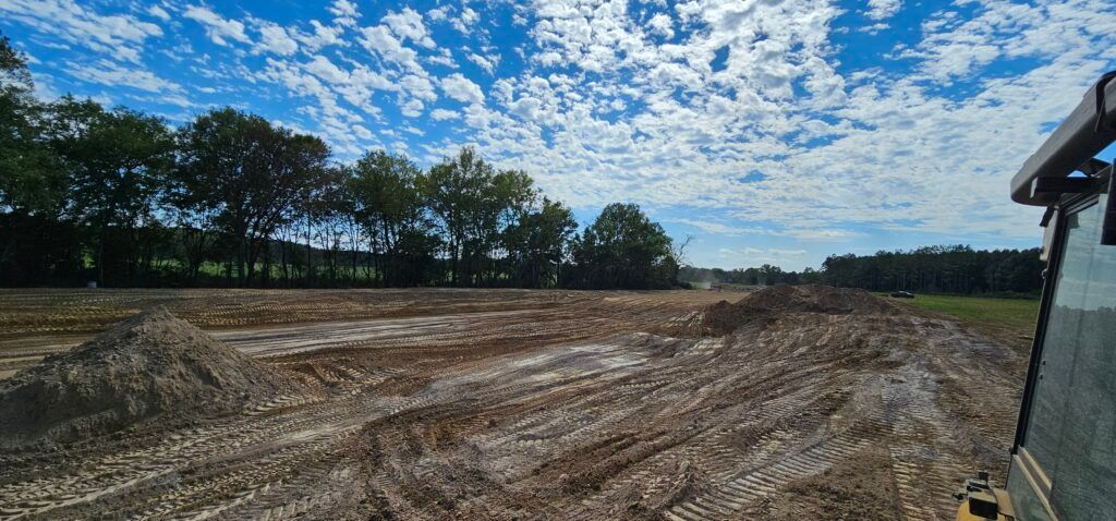 Freshly plowed field under a blue, cloud-dappled sky with trees along the horizon