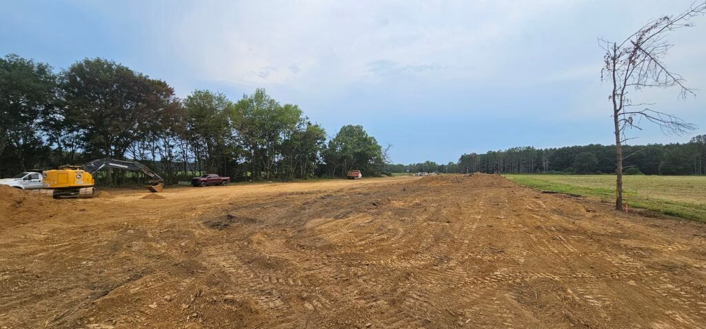Recently cleared farm field with a yellow truck, trees on the left, and cloudy sky
