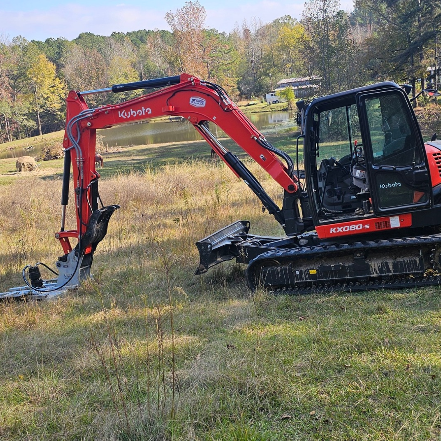 Red excavator digging in a grassy field with trees in the background