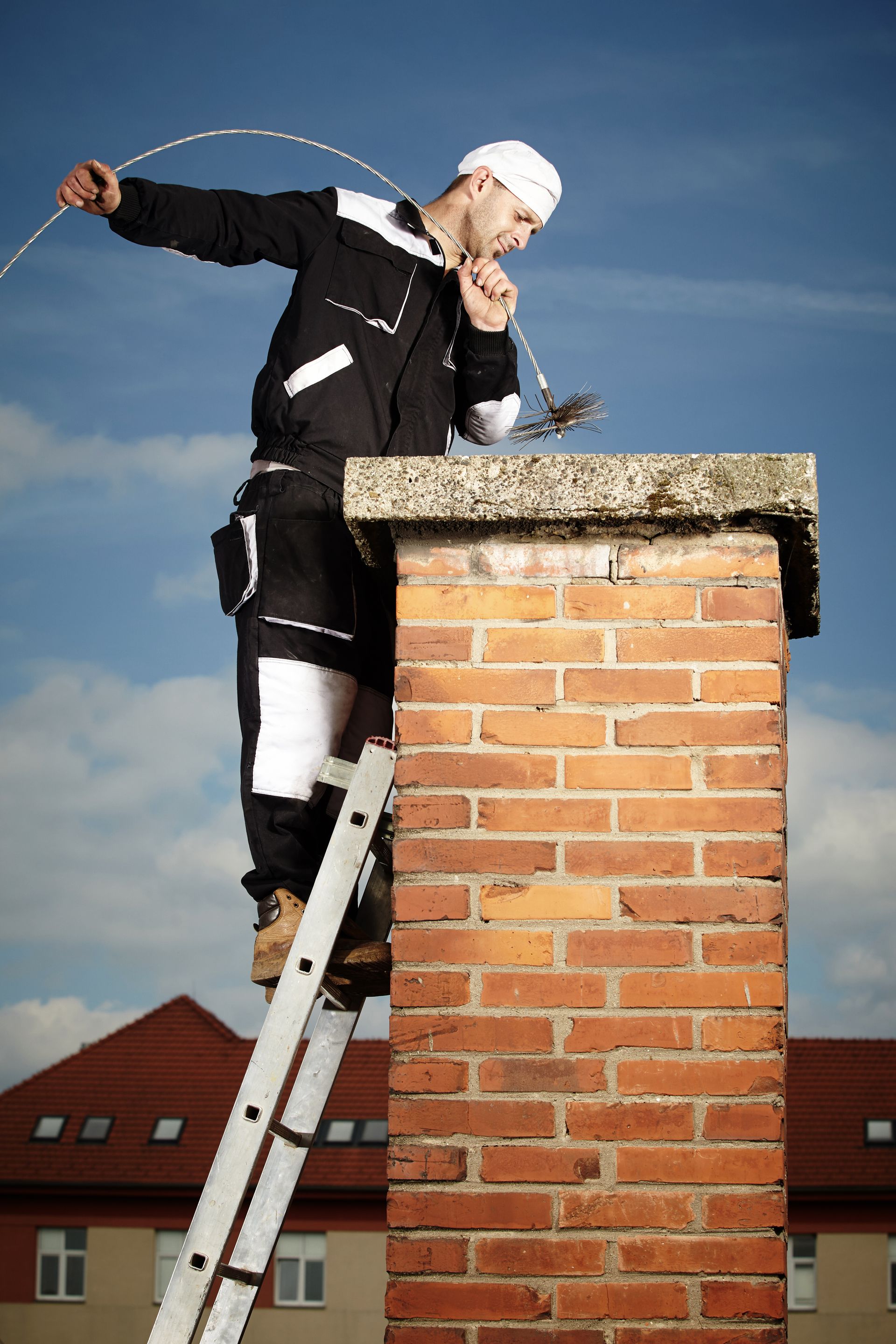 Chimney sweep on a roof using a brush to clean a chimney against a blue sky. Chimney sweep on a roof using a brush to clean a chimney against a blue sky.
