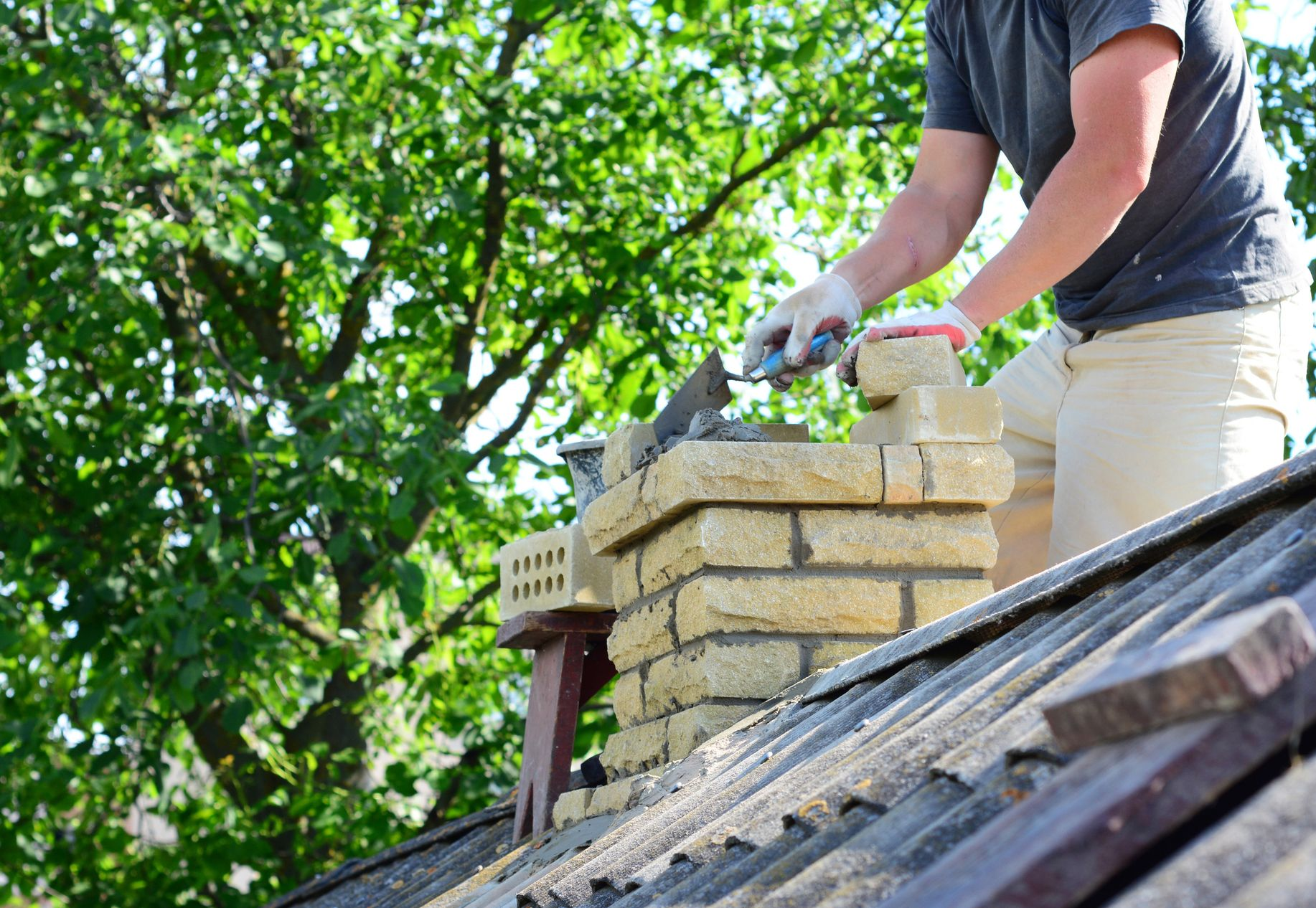 A person builds a brick chimney on a rooftop. A person builds a brick chimney on a rooftop.