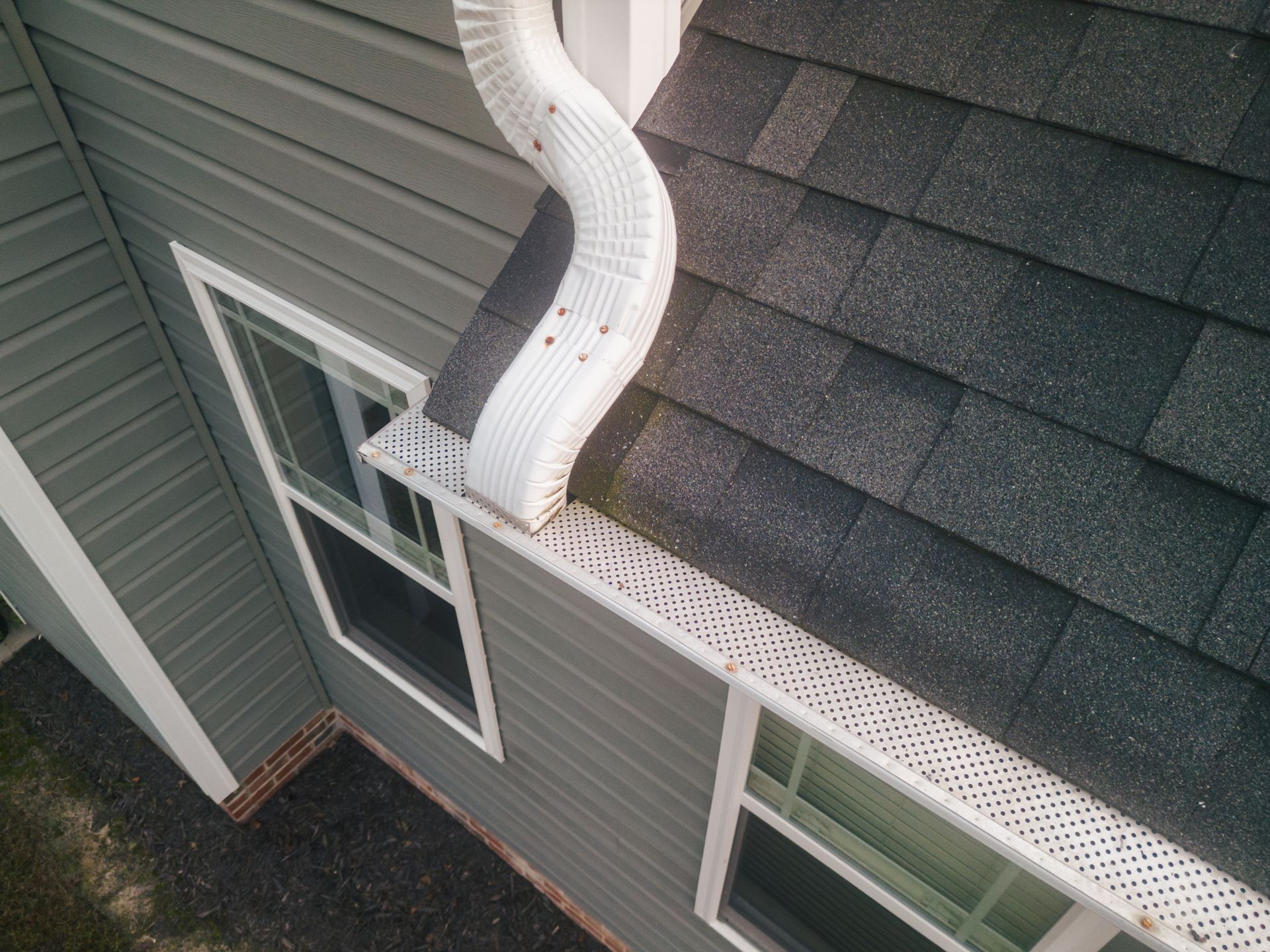 White gutters attached to a white soffit on a building with terracotta roof tiles against a cloudy sky.