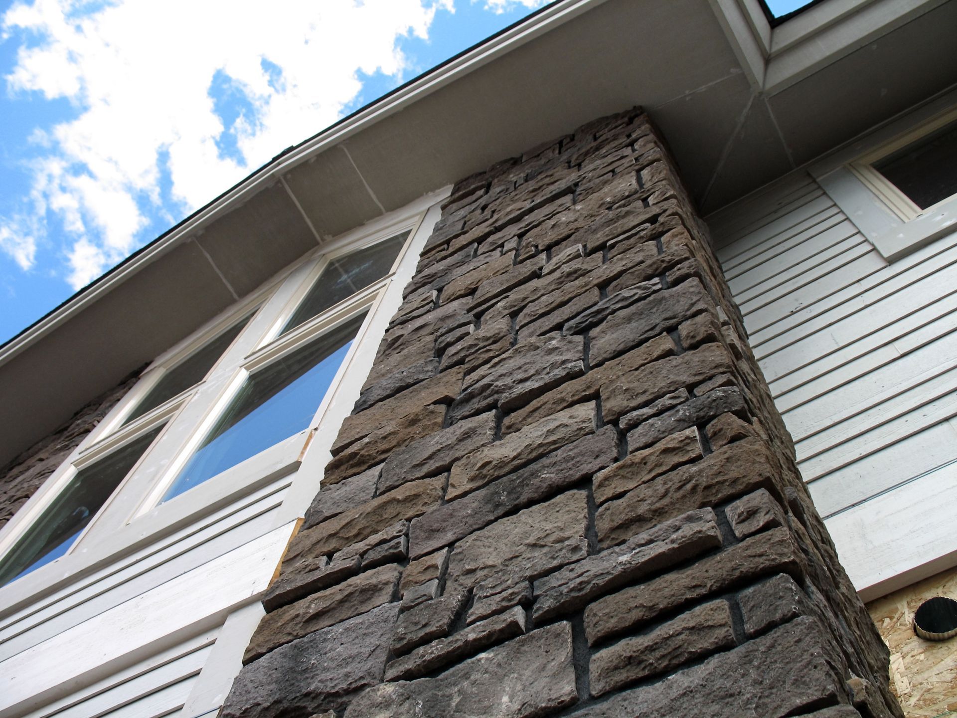 Stone pillar on a house exterior, with windows and siding; blue sky in background.