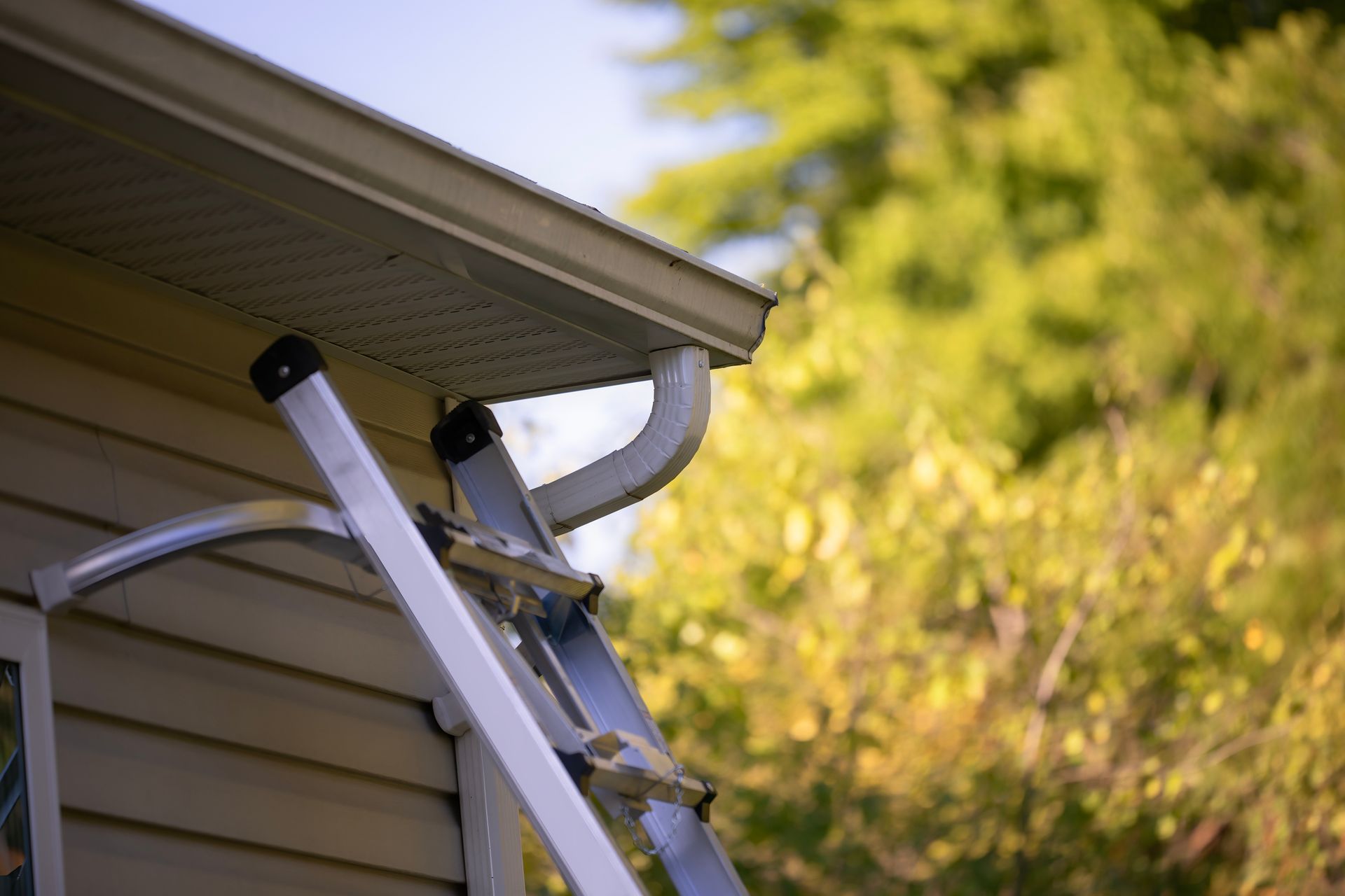 Person installing black gutter on a wooden roof with tools visible. Sunlight shines.