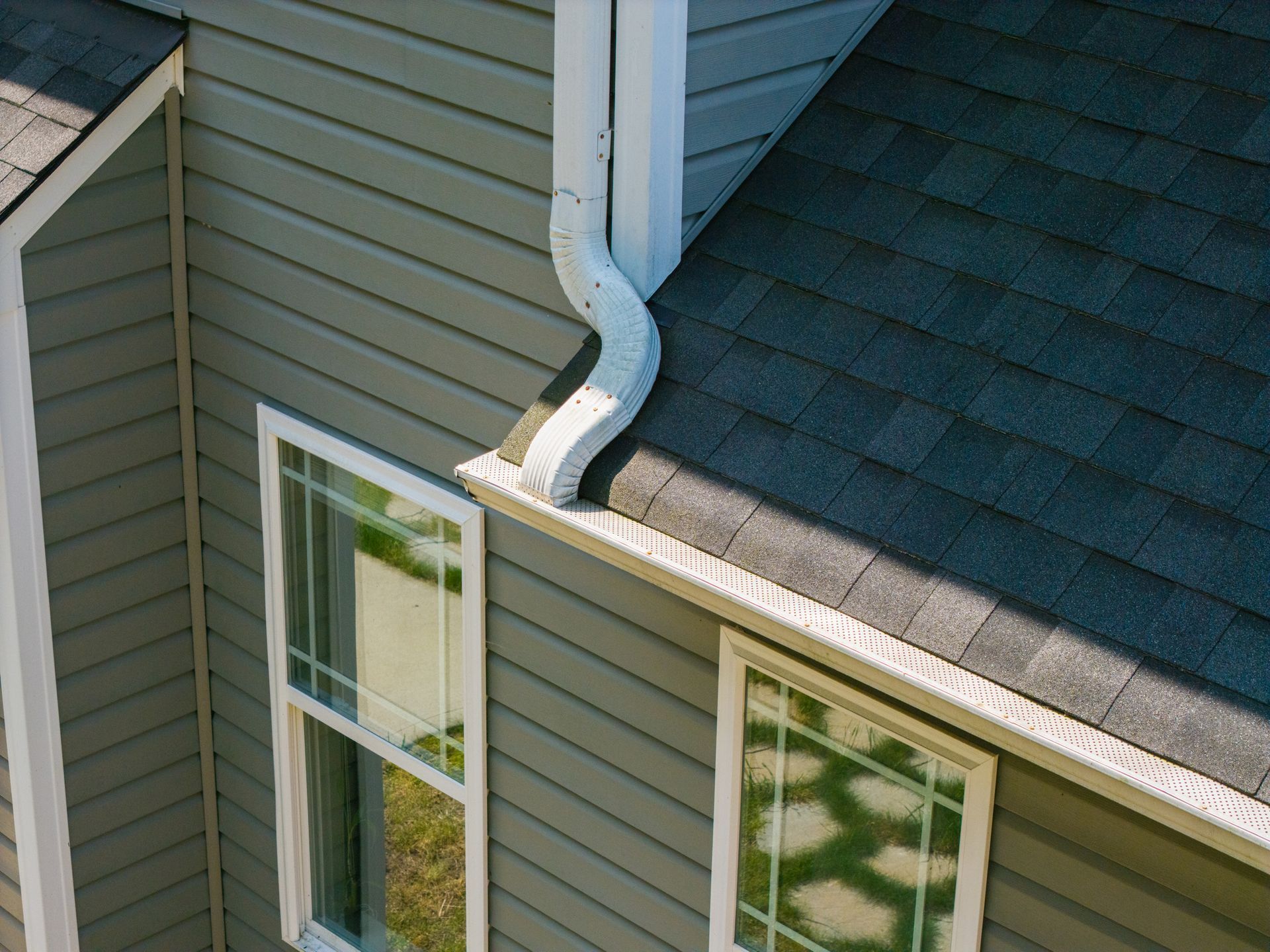 Beige house gutter and siding against a blue sky.
