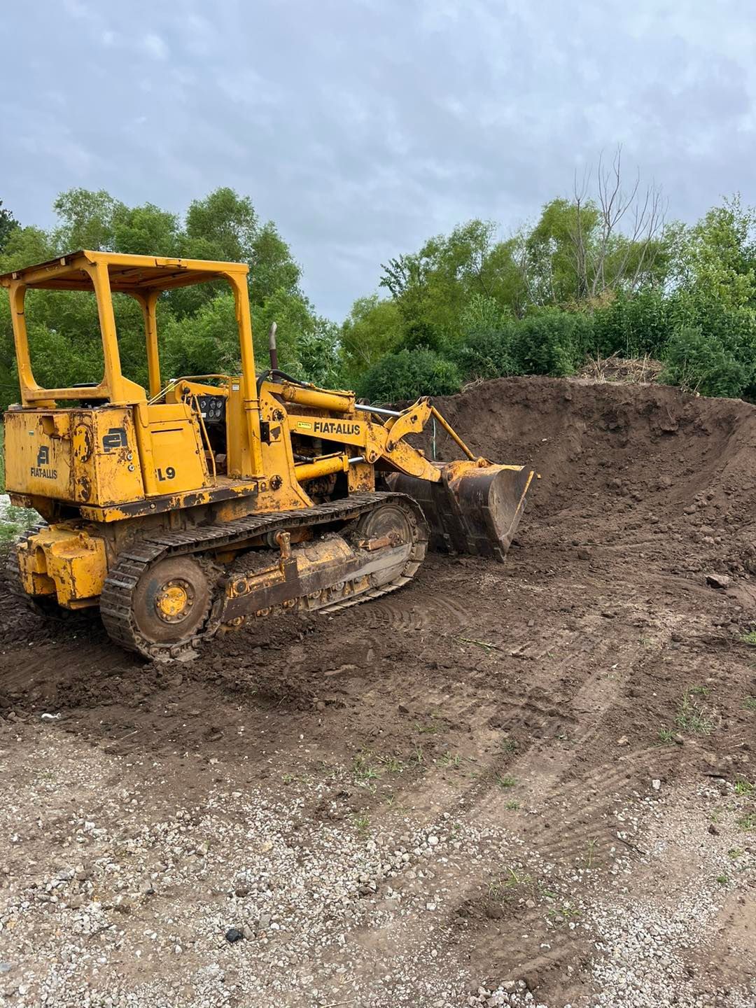 A yellow excavator is sitting on top of a pile of gravel.