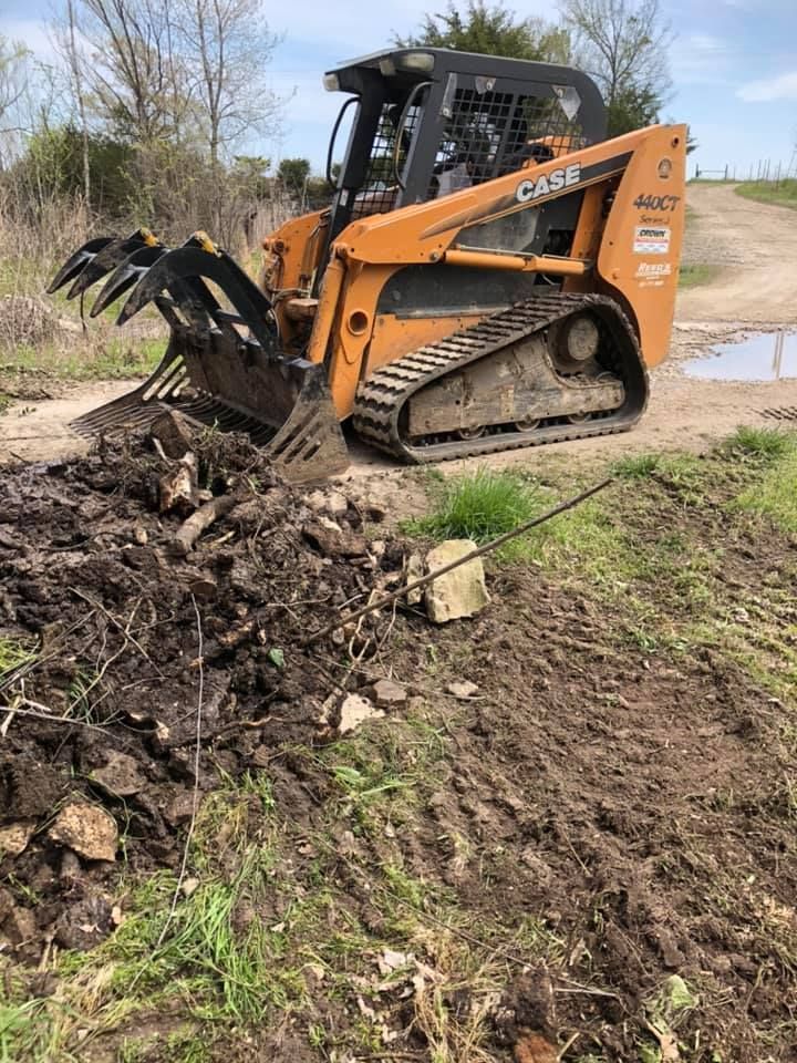 An orange Case skid steer uses a grapple to move mud and debris in a grassy area.