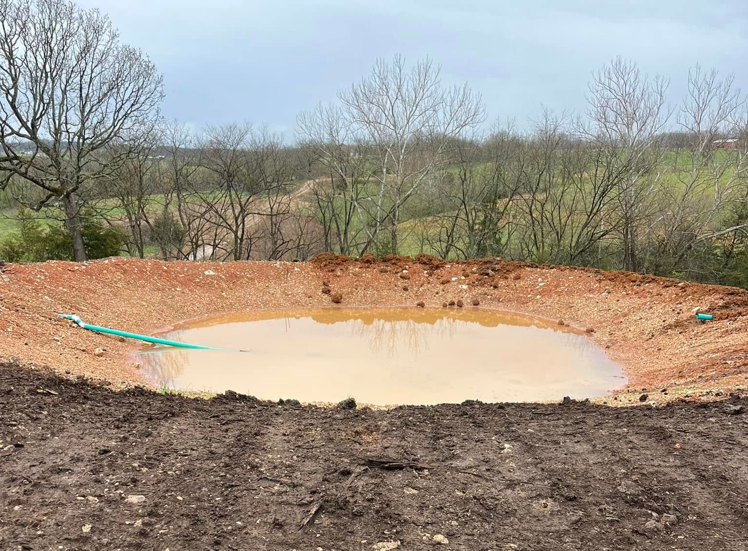 Yellow bulldozer on muddy ground, near a dirt pile, in a field with trees.
