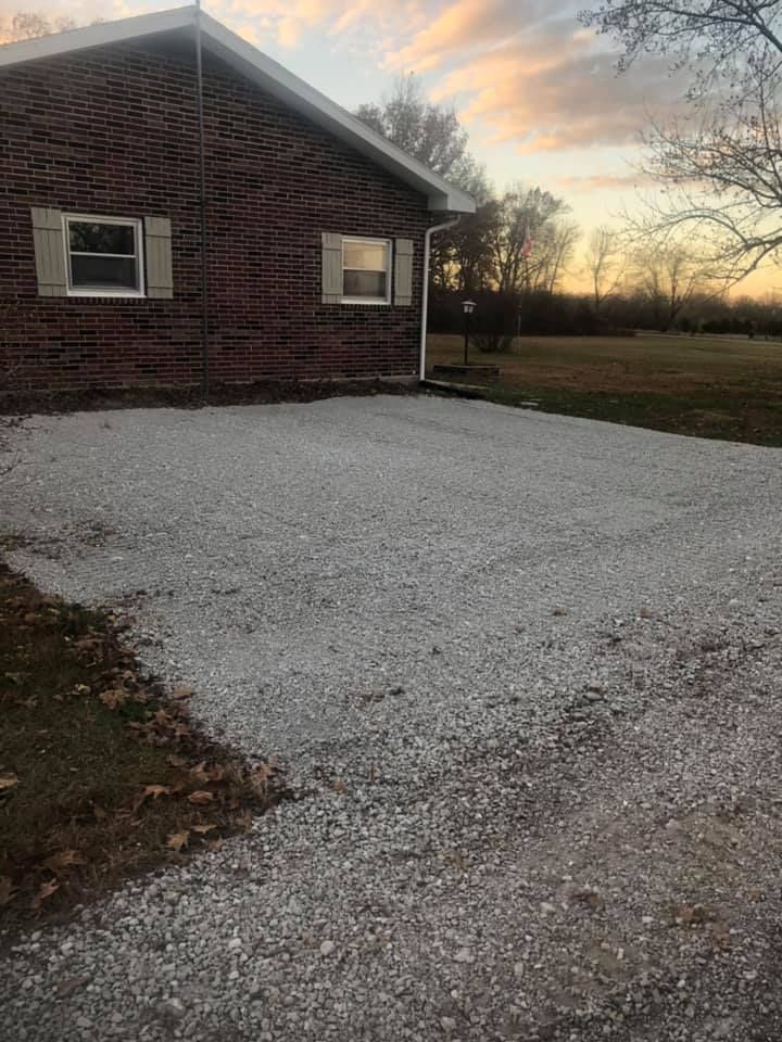 Gravel driveway in front of a brick house with small windows. A sunset is in the background.